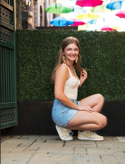 Senior girl knelling in umbrella alley in Redlands CA. 