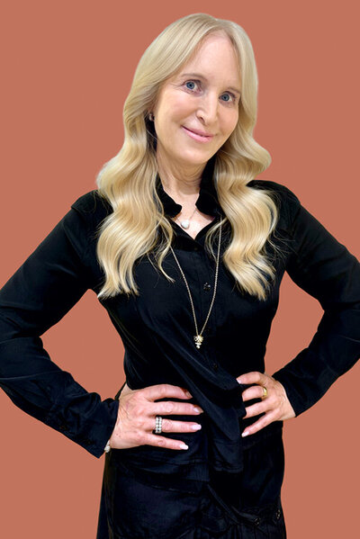 Isabella, Female hairdresser with short brunette curls, wearing a fitted black top and trousers, posing confidently.