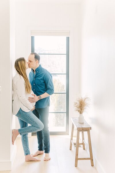 couple kiss while holding pregnant woman's belly  during maternity photo session in newton Massachusetts
