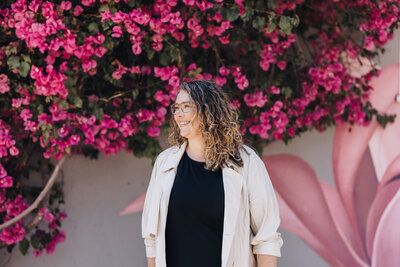 Woman stands in front of bright pink flowered bush smiling. 