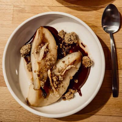 Two juicy pears rest on a plate next to a spoon, creating a charming and inviting fruit arrangement.