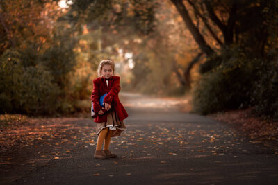 Portrait of a little girl in the park, holding a stack of books smiling at the camera.  Photo by Brittany Danielle.