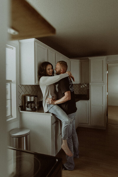 In-home session of a couple living in a tiny home. They're hanging out in their kitchen, she's on the countertop while he stands in front of her.