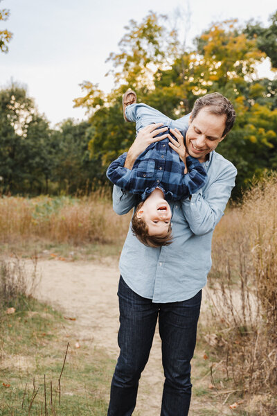 dad holding his toddler son upside down over his shoulder.  A fun moment captured during a toronto family photography session. 