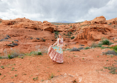 girl holding her dress out as she stands on red rock in st george for senior photos