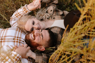 candid photo of couple laughing while laying in a field