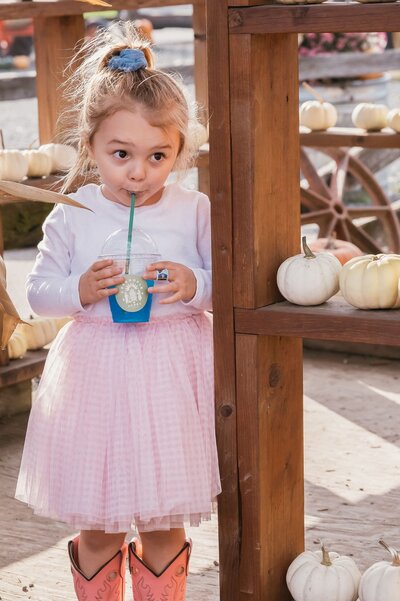 Girl dressed in a pink plaid dress sipping a blue frosty drink in a pumpkin patch store in Chilliwack, BC