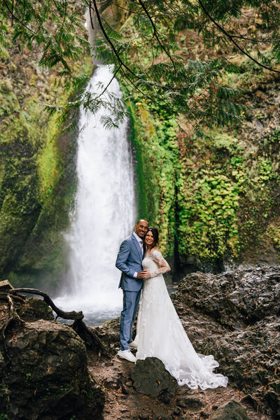 A bride and groom stand in front of a waterfall in Oregon for their Columbia River Gorge elopement.