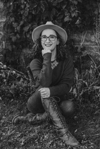 black and white portrait of Payton sitting in the grass with her legs crossed wearing a hat