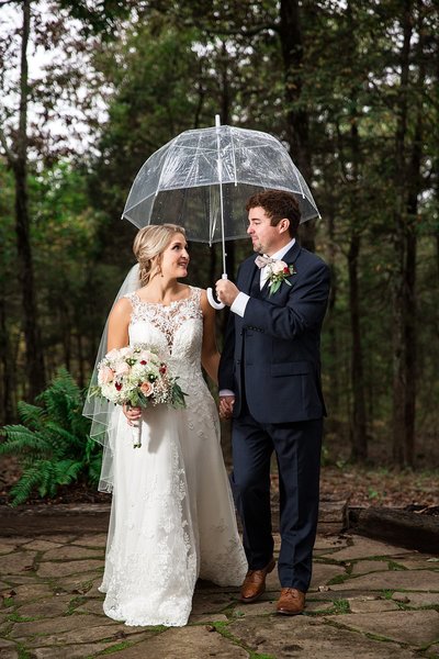 Bride and Groom holding hands and carrying umbrella during rainy wedding at the Barn at Stone Gate Farm