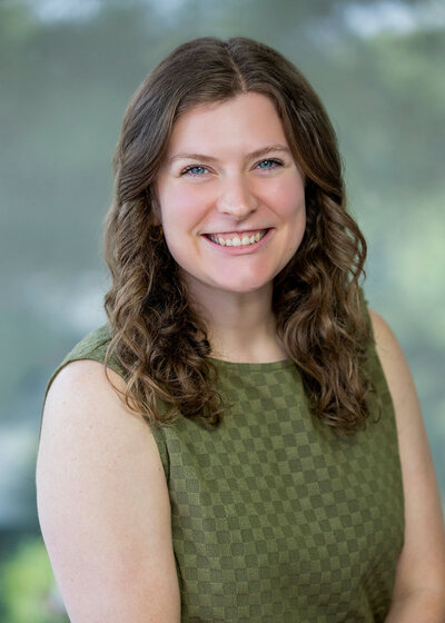 Woman in a green tank top with brown curly hair smiling against a green background