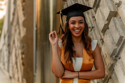 Image of graduate in her stole and cap, holding the ends of her tassel while laughing towards the camera.
