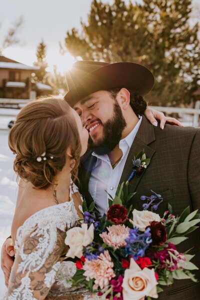 Couple go in for a kiss on their winter wedding as the bride holds a vibrant bouquet.