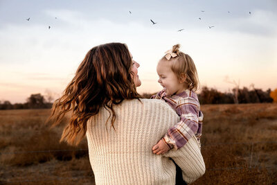 An auntie holds her niece in a field, spilling her around, while birds fly overhead