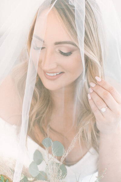 bride Smiling bride in timeless makeupwith soft smile looking at bouquet and holding veil