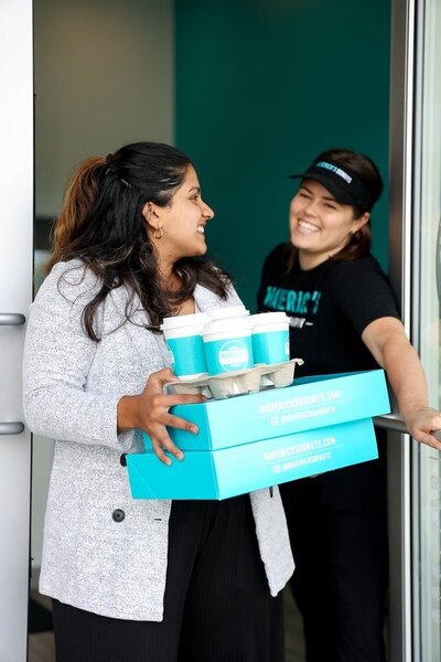 Authentic lifestyle branding image showcasing the atmosphere of a local donut shop. The photo captures the warmth of the space, the artistry of the donuts, and the joy of customers enjoying their treats, highlighting the brand’s inviting and community-focused vibe