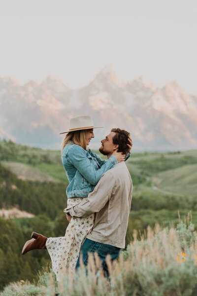 couple hugging through grass field in front of mountains