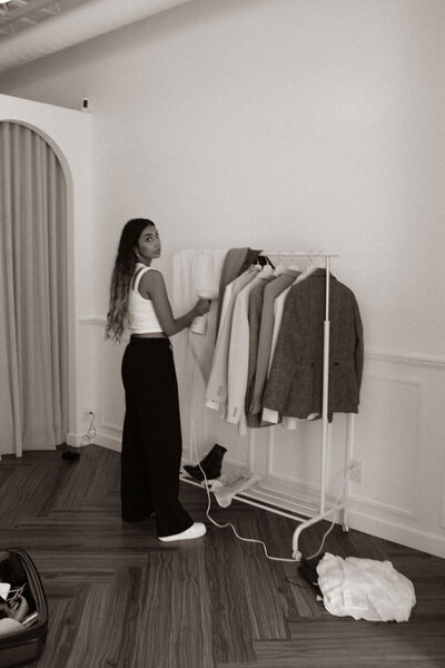 a professional businesswomen in front of a clothes rack at a photoshoot