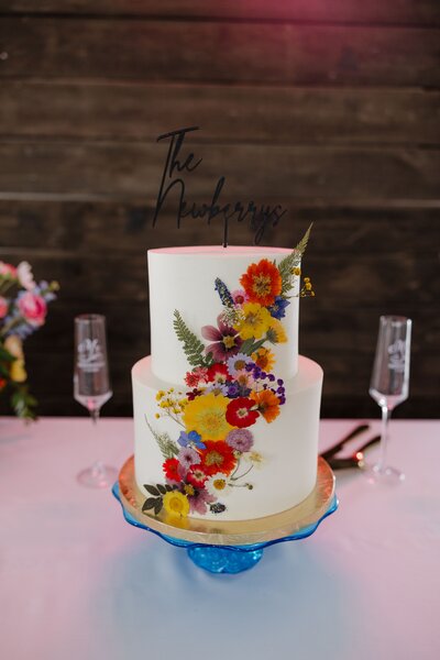 White wedding cake with teal and orange flowers on  table