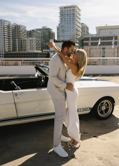 engagement couple on a rooftop garage with a classic car and elegant outfits.