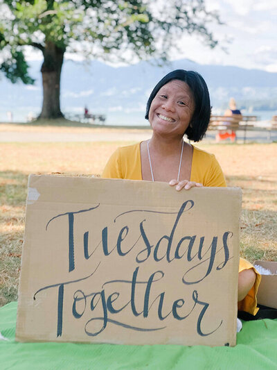 Rising Tide member holding sign saying Tuesdays Together