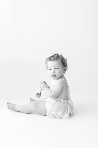 A black and white photo of ababy girl sitting on a simple, plain background during her in-studio photography session.