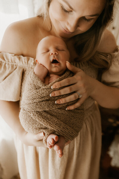 Photo of a mom holding her newborn baby all wrapped up and looking down at him in the studio.