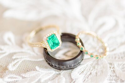 An emerald and gold wedding ring set sitting on lace.
