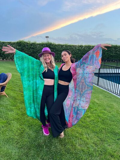 Katie Sol, spiritual entrepreneur coach, with a friend, both posing for a photo with a vibrant rainbow in the background.