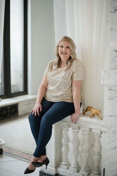 Melissa Lawrence smiles and sets atop a marble wall in a sparkly blouse