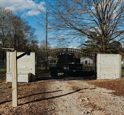 truck-driving-down-gravel-path-through-entrance-gate-under-large-tree-and-blue-skies