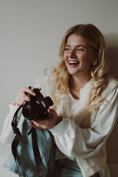  Een vrouw houdt een camera vast en glimlacht, stralend van vreugde en enthousiasme voor fotografie.