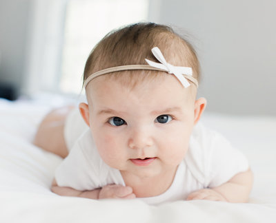 Babby laying on white bed with white bow in her hair
