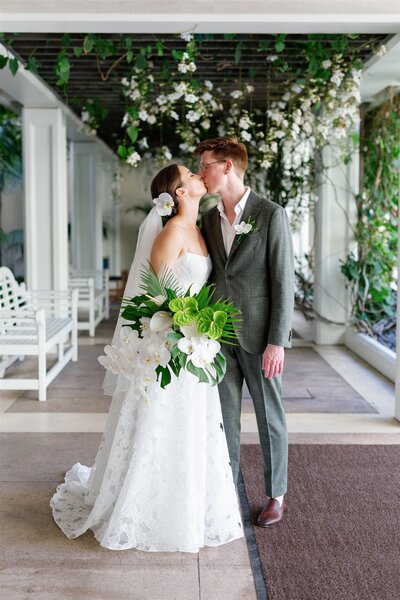 A wedding couple kissing while standing on a porch 