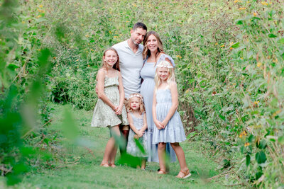 Father and pregnant mother with 3 girls surrounded by wildflowers.
