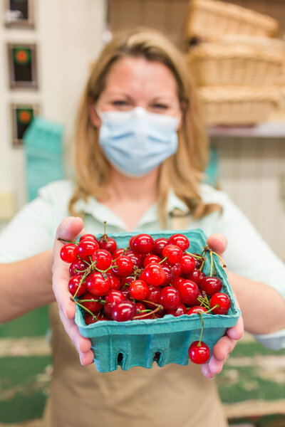 woman holding cherries in basket at farmers market