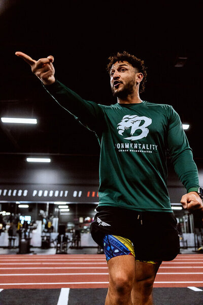 Coach in green shirt points and yells while coaching in a gym setting.