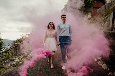 Le lendemain de leur mariage au Château de Menthon-Saint-Bernard en Haute-Savoie, les mariés marchent lors du brunch avec lunettes de soleil et fumigènes – une scène joyeuse captée par un duo photographe vidéaste