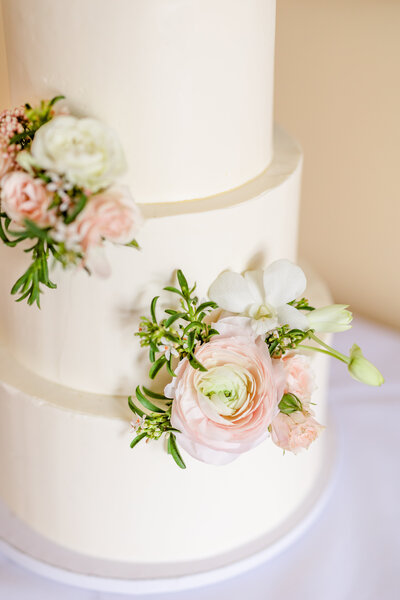 Blush ranunculus and springtime greenery on a white iced cake. Garden style floral design for wedding venues in Easton, MD, St. Michaels, MD, and Chestertown, MD.