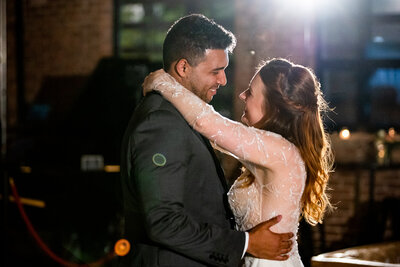 Bride in wedding gown with intricate beaded sleeves smiles at groom during first dance