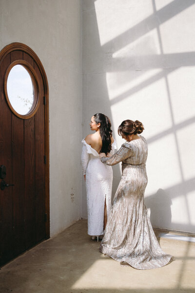 Elegant bridal getting-ready moment in natural light as mother helps bride with gown, captured in a luxury Italian wedding venue by destination photographer Madison