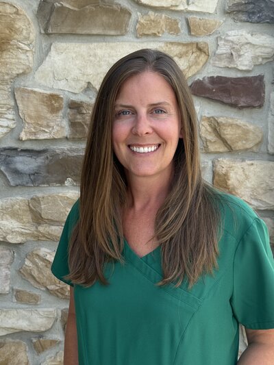 Steph Rector posing for a headshot behind a rustic stone wall. 