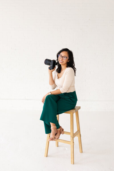 Anh Nguyen, NYC graduation photographer, smiling at the camera during a studio portrait session while sitting on a stool.