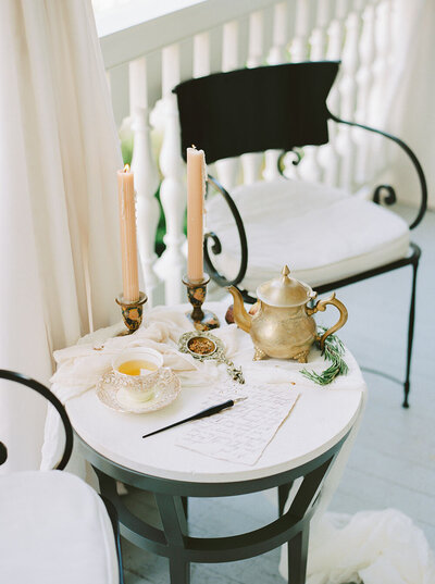 A small patio table with vintage candlesticks, herbal tea, an etched brass tea pot and calligraphed wedding vows