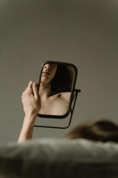 woman looking at herself in a mirror, reflecting, while sitting on the couch