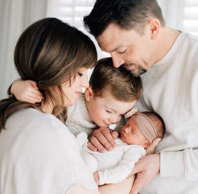 mother holding her newborn baby while dad assists and toddler hugs them