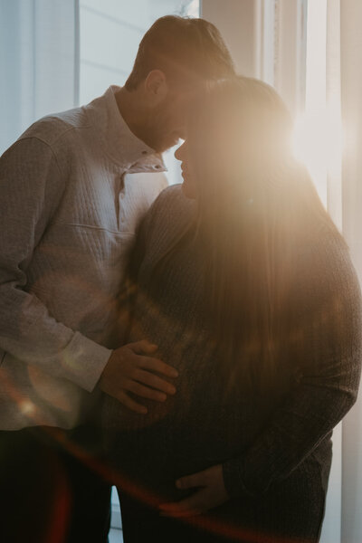 Couple embracing pregnancy belly during their couple's maternity photoshoot at their home.