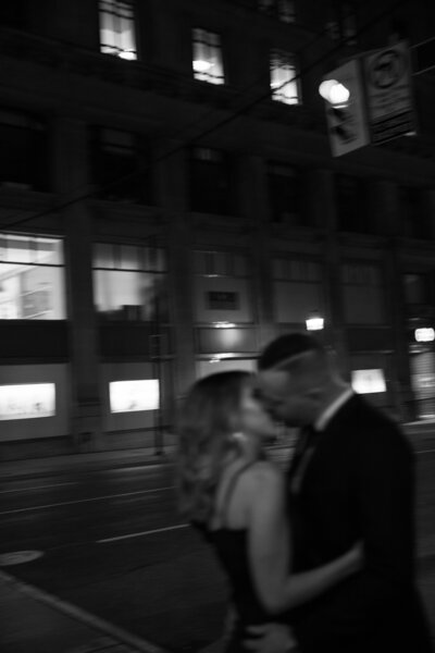 man and woman kissing on a city street at night