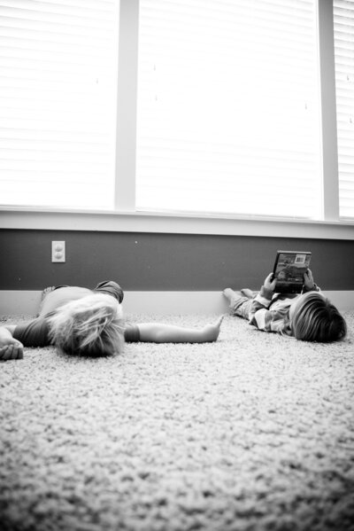 Documentary in home photography session with young boys laying on the floor near large window looking at a book black and white