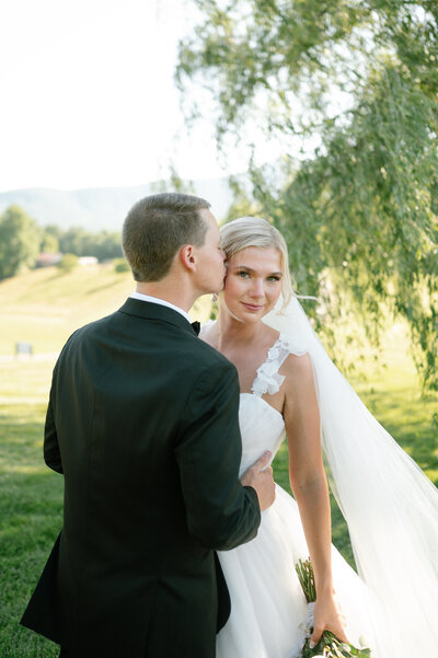 A groom gently kisses the side of his brides head